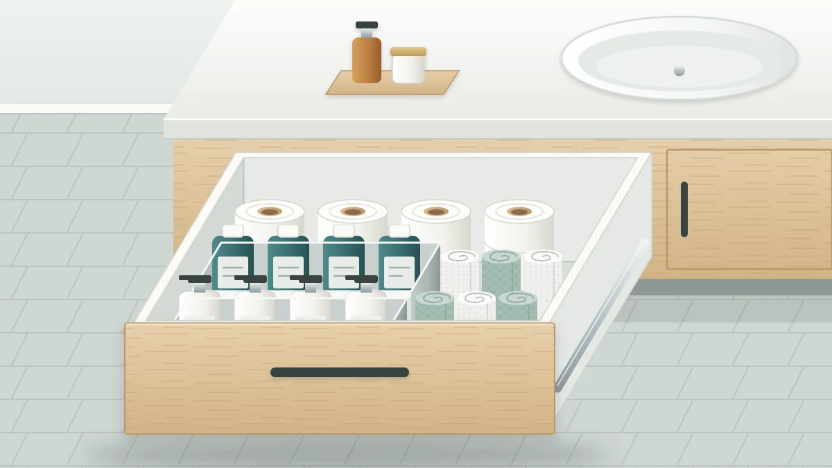 A deep vanity drawer pulled open with tall bottles upright in two rows of bins, washcloths on edge and spare toilet paper at the back