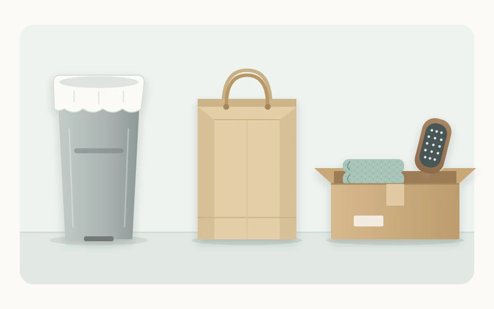 Three open containers in a row: a tall lined bin, a paper bag with handles, and a shallow box holding a hairbrush and towel