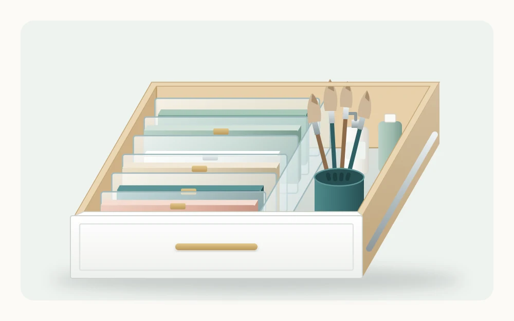 A deeper drawer with flat palettes standing on edge in a row between dividers like files, beside an upright cup of brushes