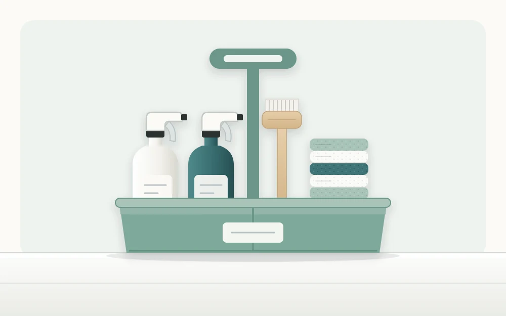 A cleaning caddy with a center handle holding two spray bottles, a scrub brush and a stack of folded cloths on a plain counter